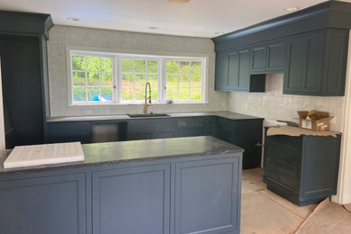 Mid-sized elegant l-shaped light wood floor laundry room photo in Portland with an undermount sink, shaker cabinets, blue cabinets, soapstone countertops, white backsplash, marble backsplash and black countertops