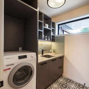 Modern inredning av en beige beige tvättstuga enbart för tvätt, med en enkel diskho, släta luckor, bruna skåp, laminatbänkskiva, grönt stänkskydd, stänkskydd i keramik, klinkergolv i keramik och en tvättpelare