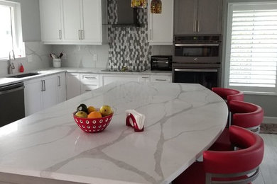 This is an example of a mid-sized modern l-shaped open plan kitchen in Miami with shaker cabinets, quartzite benchtops, grey splashback, glass tile splashback, with island and white benchtop.