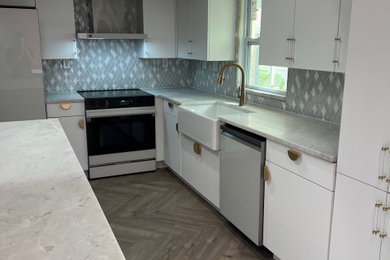 Inspiration for a mid-sized modern vinyl floor and brown floor eat-in kitchen remodel in Tampa with a farmhouse sink, flat-panel cabinets, white cabinets, marble countertops, gray backsplash, glass tile backsplash, white appliances, an island and white countertops