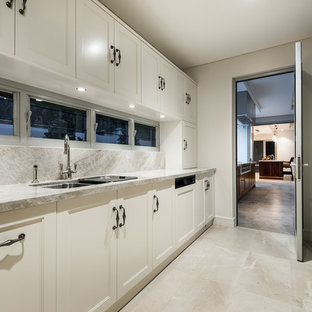 Modern inredning av ett stort kök, med en dubbel diskho, luckor med infälld panel, vita skåp, marmorbänkskiva, vitt stänkskydd, stänkskydd i stenkakel, integrerade vitvaror och marmorgolv