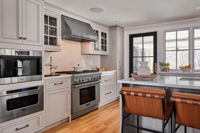 Example of a transitional light wood floor and brown floor kitchen design in Providence with recessed-panel cabinets, gray cabinets, white backsplash, marble backsplash, stainless steel appliances and white countertops