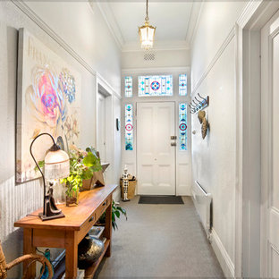 Inredning av en eklektisk hall, med vita väggar, en enkeldörr, en vit dörr och grått golv