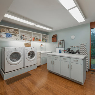 他の地域の大きいミッドセンチュリースタイルのおしゃれな洗濯室 (青い壁、左右配置の洗濯機・乾燥機、ダブルシンク、オープンシェルフ、白いキャビネット、グレーのキッチンカウンター、コルクフローリング) の写真