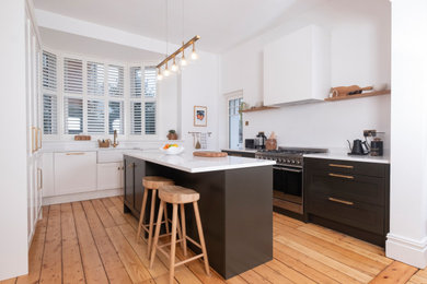 Design ideas for a medium sized classic cream and black u-shaped kitchen/diner in Cardiff with a belfast sink, shaker cabinets, black cabinets, quartz worktops, light hardwood flooring, an island, white worktops and feature lighting.