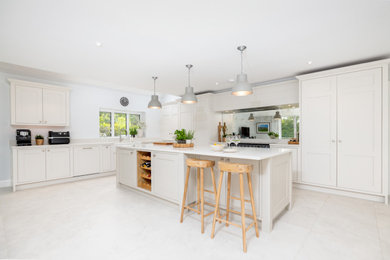 Photo of a contemporary l-shaped kitchen/diner in Berkshire with shaker cabinets, beige cabinets, engineered stone countertops, metallic splashback, mirror splashback, limestone flooring, an island, beige floors and white worktops.