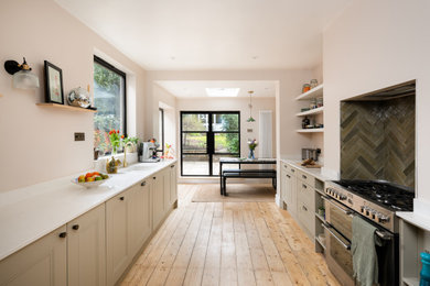 Design ideas for a large classic galley kitchen/diner in Gloucestershire with an integrated sink, beaded cabinets, green cabinets, engineered stone countertops, green splashback, ceramic splashback, stainless steel appliances, medium hardwood flooring, no island, brown floors and white worktops.