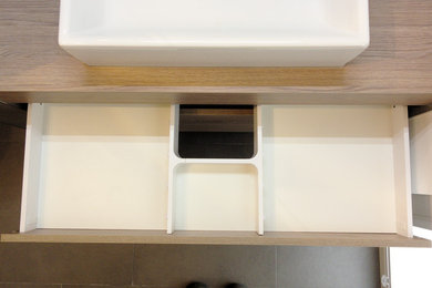 Kleines Modernes Badezimmer En Suite mit flächenbündigen Schrankfronten, hellbraunen Holzschränken, grauen Fliesen, Steinfliesen, weißer Wandfarbe, Porzellan-Bodenfliesen, Aufsatzwaschbecken, Waschtisch aus Holz, grauem Boden und Falttür-Duschabtrennung in Nürnberg