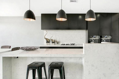 This is an example of a small contemporary galley eat-in kitchen in Melbourne with flat-panel cabinets, quartz benchtops, with island, an undermount sink, black cabinets, white splashback, stone slab splashback, black appliances, porcelain floors, grey floor and yellow benchtop.
