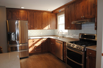 Example of a mid-sized classic l-shaped light wood floor enclosed kitchen design in Cleveland with a double-bowl sink, shaker cabinets, medium tone wood cabinets, quartzite countertops, white backsplash, subway tile backsplash, stainless steel appliances and an island