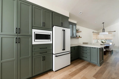Example of a transitional vinyl floor, brown floor and vaulted ceiling kitchen design in Orange County with a single-bowl sink, shaker cabinets, green cabinets, white backsplash, white appliances, a peninsula and white countertops