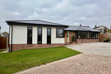 Design ideas for a medium sized and beige modern bungalow render and front house exterior in Essex with a hip roof, a tiled roof and a black roof.