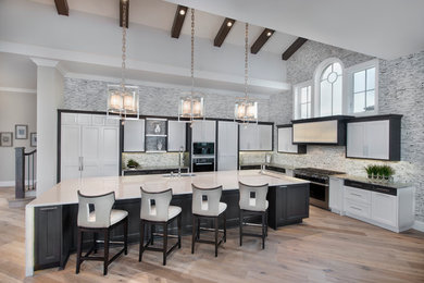 Example of a huge minimalist l-shaped medium tone wood floor open concept kitchen design in Miami with a farmhouse sink, white cabinets, gray backsplash, stone tile backsplash, paneled appliances and an island