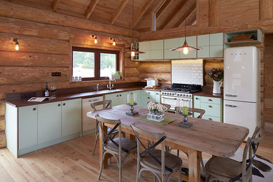 Design ideas for a mid-sized country l-shaped eat-in kitchen in Christchurch with a drop-in sink, flat-panel cabinets, green cabinets, wood benchtops, white splashback, ceramic splashback, white appliances, light hardwood floors and no island.