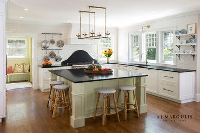 This is an example of a mid-sized traditional u-shaped open plan kitchen in Philadelphia with an undermount sink, beaded inset cabinets, white cabinets, soapstone benchtops, white splashback, ceramic splashback, stainless steel appliances, dark hardwood floors, with island, brown floor and black benchtop.