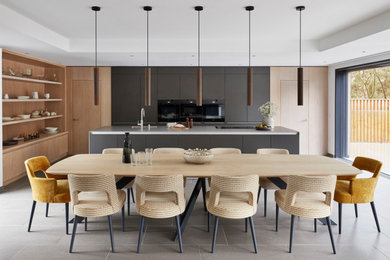 This is an example of an expansive contemporary single-wall open plan kitchen in Hampshire with an integrated sink, flat-panel cabinets, black cabinets, stainless steel benchtops, black appliances, porcelain floors, with island and grey floor.