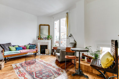 Cette image montre un salon traditionnel de taille moyenne et ouvert avec une bibliothèque ou un coin lecture, un mur blanc, un sol en bois brun, une cheminée d'angle, un manteau de cheminée en pierre, aucun téléviseur et un sol marron.