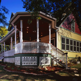 Пример оригинального дизайна интерьера: двухэтажный фасад дома желтого цвета в викторианском стиле с облицовкой из дерева