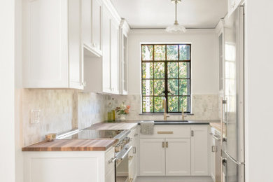 Enclosed kitchen - small traditional galley light wood floor, brown floor and vaulted ceiling enclosed kitchen idea in Portland with a farmhouse sink, recessed-panel cabinets, white cabinets, wood countertops, gray backsplash, stone tile backsplash, stainless steel appliances, no island and brown countertops