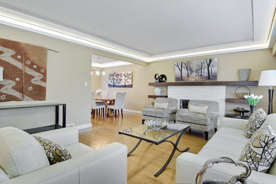 This is an example of a mid-sized contemporary open concept family room in Vancouver with beige walls, light hardwood floors, a standard fireplace, a brick fireplace surround, no tv and brown floor.