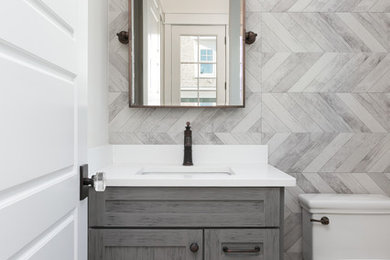 Small country gray tile and porcelain tile medium tone wood floor and gray floor powder room photo in Charleston with flat-panel cabinets, gray cabinets, a one-piece toilet, white walls, an undermount sink, quartz countertops and white countertops