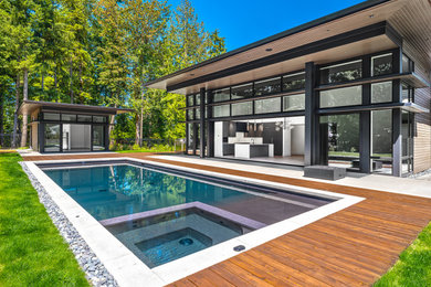 Modelo de casa de la piscina y piscina moderna rectangular en patio trasero con entablado