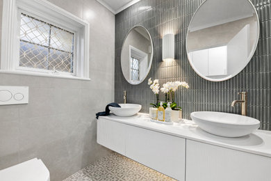 Photo of a mid-sized 3/4 bathroom in Sydney with beaded inset cabinets, white cabinets, an alcove shower, a one-piece toilet, multi-coloured tile, ceramic tile, multi-coloured walls, ceramic floors, a vessel sink, solid surface benchtops, grey floor, an open shower, white benchtops, a double vanity, a floating vanity and timber.