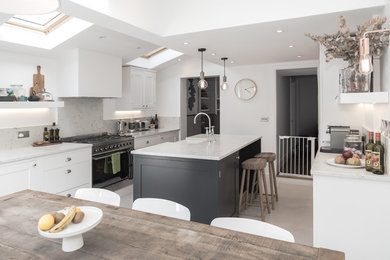 Photo of a small contemporary eat-in kitchen in London with a farmhouse sink, shaker cabinets, white cabinets, marble benchtops, marble splashback, stainless steel appliances, a peninsula and beige floor.
