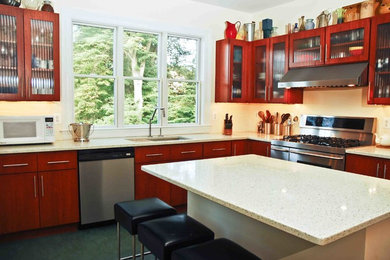 Mid-sized trendy l-shaped slate floor enclosed kitchen photo in Baltimore with a drop-in sink, glass-front cabinets, medium tone wood cabinets, solid surface countertops, stainless steel appliances and an island
