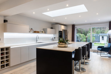 This is an example of a mid-sized contemporary single-wall eat-in kitchen in Sussex with flat-panel cabinets, engineered quartz splashback and with island.