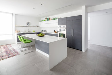 This is an example of a large modern l-shaped open plan kitchen in Los Angeles with a double-bowl sink, flat-panel cabinets, dark wood cabinets, quartz benchtops, white splashback, stainless steel appliances, porcelain floors and with island.