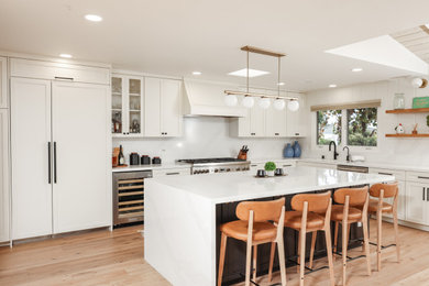 Large trendy l-shaped light wood floor, brown floor and exposed beam open concept kitchen photo in San Diego with an undermount sink, shaker cabinets, beige cabinets, quartz countertops, white backsplash, quartz backsplash, stainless steel appliances, an island and white countertops