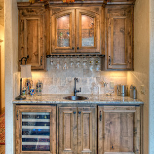 他の地域の中サイズのトラディショナルスタイルのおしゃれなウェットバー (ドロップインシンク、落し込みパネル扉のキャビネット、中間色木目調キャビネット、御影石カウンター、ベージュキッチンパネル、濃色無垢フローリング、トラバーチンの床) の写真
