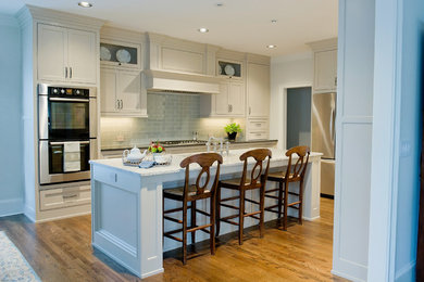 Open concept kitchen - mid-sized traditional l-shaped medium tone wood floor open concept kitchen idea in Atlanta with an undermount sink, shaker cabinets, white cabinets, marble countertops, blue backsplash, glass tile backsplash, stainless steel appliances and an island