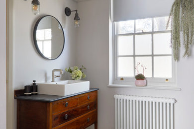 Mittelgroßes Klassisches Badezimmer mit hellbraunen Holzschränken, weißen Fliesen, Quarzit-Waschtisch, schwarzer Waschtischplatte, Einzelwaschbecken, freistehendem Waschtisch, bodengleicher Dusche, Waschtischkonsole und Falttür-Duschabtrennung in Hertfordshire