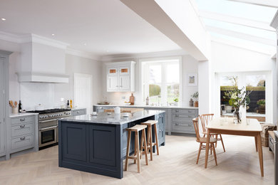 Design ideas for a medium sized contemporary l-shaped open plan kitchen in Cornwall with a built-in sink, shaker cabinets, brown cabinets, quartz worktops, white splashback, glass tiled splashback, stainless steel appliances, light hardwood flooring, an island, brown floors, white worktops and all types of ceiling.