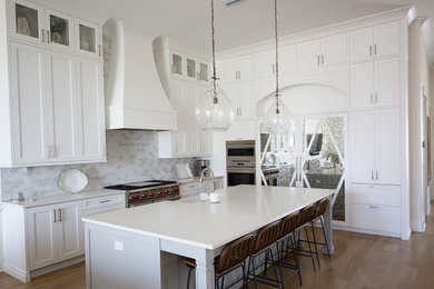 Inspiration for a large transitional l-shaped medium tone wood floor, beige floor and tray ceiling eat-in kitchen remodel in Miami with a farmhouse sink, shaker cabinets, white cabinets, quartzite countertops, white backsplash, ceramic backsplash, stainless steel appliances, an island and white countertops