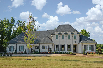 Large transitional two-storey stucco beige house exterior in Other with a hip roof and a shingle roof.