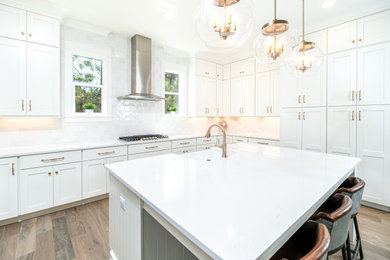 Inspiration for a mid-sized transitional u-shaped brown floor kitchen remodel with a farmhouse sink, recessed-panel cabinets, white cabinets, white backsplash, stainless steel appliances, an island and white countertops