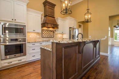 Example of a large classic single-wall dark wood floor kitchen design with an undermount sink, recessed-panel cabinets, white cabinets, granite countertops, beige backsplash, stone tile backsplash, stainless steel appliances and an island