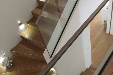 Mid-sized contemporary wood u-shaped staircase in Paris with glass risers and glass railing.