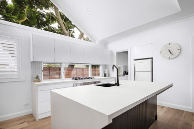 Design ideas for a mid-sized single-wall eat-in kitchen in Sydney with a drop-in sink, flat-panel cabinets, white cabinets, laminate benchtops, glass sheet splashback, light hardwood floors, with island, brown floor and white benchtop.