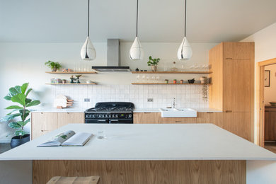 Inspiration for a mid-sized scandinavian single-wall eat-in kitchen in London with a double-bowl sink, flat-panel cabinets, medium wood cabinets, solid surface benchtops, white splashback, ceramic splashback, black appliances, porcelain floors, with island, grey floor and white benchtop.