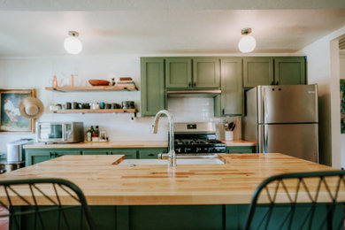 Ejemplo de cocina pequeña con puertas de armario verdes, encimera de madera, salpicadero blanco, salpicadero de azulejos de cerámica, electrodomésticos de acero inoxidable y una isla