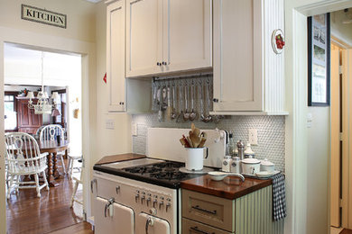 Example of a mid-sized ornate u-shaped medium tone wood floor enclosed kitchen design in Other with shaker cabinets, wood countertops, a farmhouse sink, white cabinets, blue backsplash, glass tile backsplash, white appliances and an island