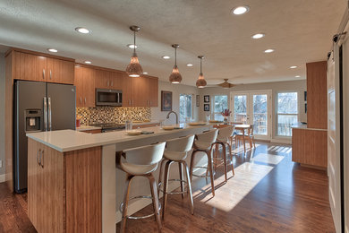 This is an example of a large midcentury single-wall open plan kitchen in Denver with an undermount sink, flat-panel cabinets, light wood cabinets, solid surface benchtops, multi-coloured splashback, mosaic tile splashback, stainless steel appliances, dark hardwood floors, with island and brown floor.