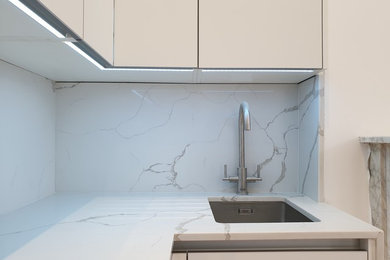 Design ideas for a medium sized contemporary l-shaped open plan kitchen in London with a built-in sink, flat-panel cabinets, white cabinets, quartz worktops, white splashback, stone slab splashback, integrated appliances, laminate floors, no island, brown floors and white worktops.