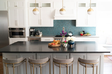 Transitional dark wood floor and brown floor kitchen photo in Dallas with a drop-in sink, glass-front cabinets, white cabinets, blue backsplash, stainless steel appliances, an island and black countertops