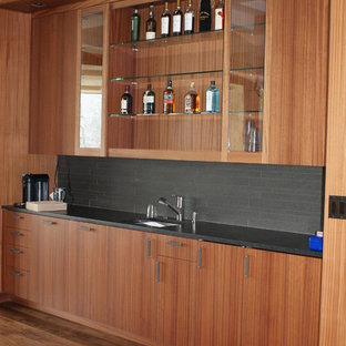 デンバーの中サイズのコンテンポラリースタイルのおしゃれなウェットバー (アンダーカウンターシンク、フラットパネル扉のキャビネット、中間色木目調キャビネット、黒いキッチンパネル、人工大理石カウンター、セラミックタイルのキッチンパネル、濃色無垢フローリング) の写真