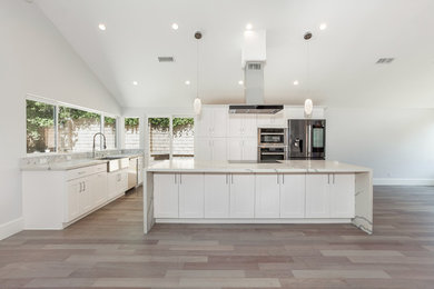 Eat-in kitchen - mid-sized modern single-wall light wood floor and brown floor eat-in kitchen idea in Los Angeles with a farmhouse sink, shaker cabinets, white cabinets, quartz countertops, marble backsplash, stainless steel appliances, an island and white countertops